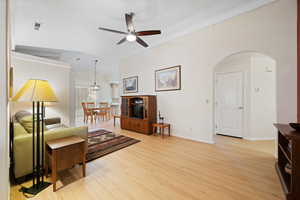 Living room featuring vaulted ceiling, light wood-style floors, ornamental molding, ceiling fan, and arched walkways