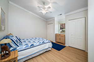 Bedroom featuring multiple closets, light wood-style flooring, a ceiling fan, and crown molding
