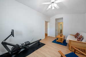 Workout area with light wood-style floors, vaulted ceiling, and ceiling fan