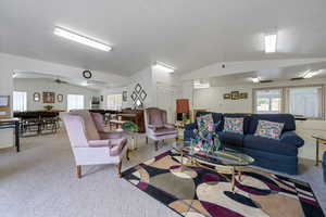 Living area with vaulted ceiling, light colored carpet, a ceiling fan, and a textured ceiling