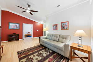 Living room featuring crown molding, light wood-style flooring, vaulted ceiling, and ceiling fan