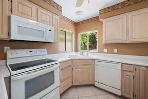 Kitchen with light brown cabinets, white appliances, light countertops, light tile patterned flooring, and a ceiling fan