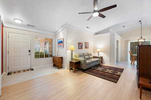 Living room featuring ornamental molding, light wood-type flooring, a ceiling fan, a chandelier, and lofted ceiling
