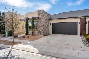 Modern home featuring driveway, stucco siding, stone siding, a tiled roof, and an attached garage