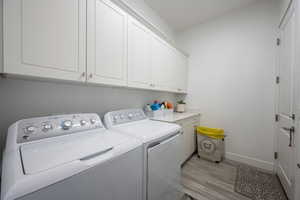 Laundry room featuring light wood-type flooring, cabinet space, and washing machine and clothes dryer