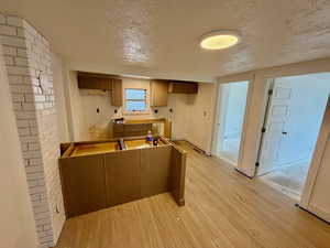 Kitchen with a textured ceiling, light wood finished floors, and brown cabinets