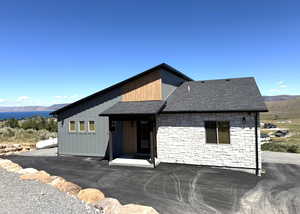 View of front of home featuring a mountain view, stone siding, and a shingled roof