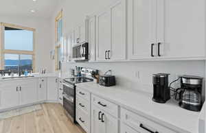 Kitchen with appliances with stainless steel finishes, white cabinets, light wood-style flooring, light stone counters, and a mountain view