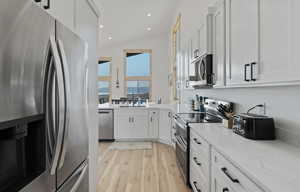 Kitchen with appliances with stainless steel finishes, light wood-style flooring, white cabinets, recessed lighting, and light stone counters