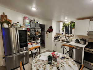 Kitchen with stainless steel appliances, white cabinetry, light countertops, light wood-type flooring, and under cabinet range hood