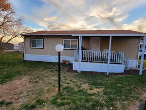 Back of property at dusk with a lawn, roof with shingles, and a porch
