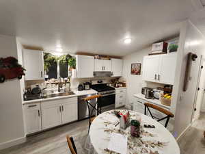 Kitchen with appliances with stainless steel finishes, white cabinetry, light countertops, light wood-style flooring, and lofted ceiling