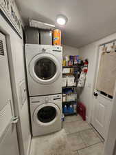 Laundry room featuring a textured ceiling, stacked washer / dryer, a heating unit, and light tile patterned floors