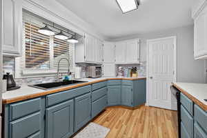 Kitchen with tasteful backsplash, light countertops, stainless steel appliances, painted cabinetry, and light wood-style flooring
