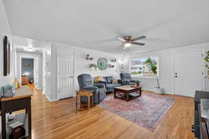 Living room featuring light paint, hardwood flooring, and a ceiling fan