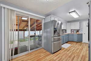 Kitchen with tasteful backsplash, light countertops, stainless steel appliances, painted cabinetry, and light wood-style flooring