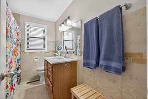 Full bathroom with tile walls, vanity, light tile floors, and a tub/shower combo