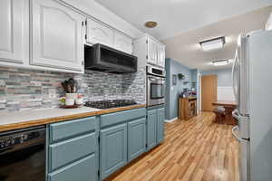 Kitchen with tasteful backsplash, light countertops, stainless steel appliances, painted cabinetry, and light wood-style flooring