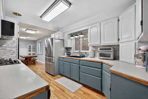 Kitchen with tasteful backsplash, light countertops, stainless steel appliances, painted cabinetry, and light wood-style flooring