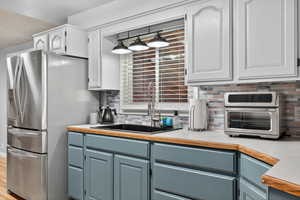 Kitchen with tasteful backsplash, light countertops, stainless steel appliances, painted cabinetry, and light wood-style flooring