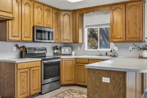 Kitchen featuring a peninsula, stainless steel appliances, brown cabinets, and light countertops