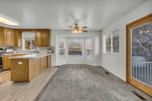 Kitchen featuring brown cabinets, light countertops, a peninsula, ceiling fan, and light colored carpet