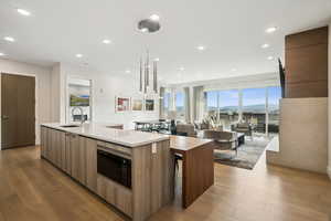 Kitchen with modern cabinets, light wood-style floors, decorative light fixtures, stainless steel microwave, and recessed lighting
