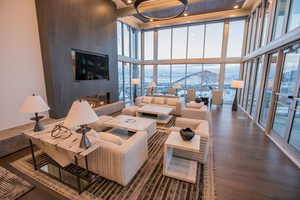 Living room with a large fireplace, a wall of windows, a towering ceiling, recessed lighting, and wood finished floors