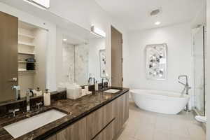 Bathroom featuring double vanity, a freestanding tub, a marble finish shower, and light tile patterned floors