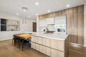 Kitchen with white cabinetry, light wood-type flooring, an island with sink, backsplash, and modern cabinets