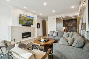 Living room with a barn door, recessed lighting, a premium fireplace, and wood finished floors