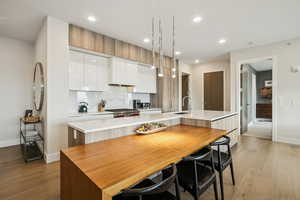 Kitchen featuring a center island with sink, white cabinets, light wood-type flooring, tasteful backsplash, and modern cabinets