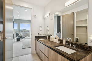 Full bath featuring light colored carpet, light tile patterned flooring, double vanity, recessed lighting, and a spacious closet