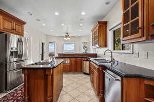 Kitchen featuring glass insert cabinets, appliances with stainless steel finishes, brown cabinets, an island with sink, and recessed lighting