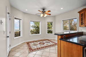 Kitchen with dark stone countertops, glass insert cabinets, brown cabinetry, light tile patterned flooring, and recessed lighting