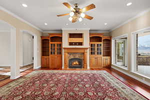 Living area with dark wood-style flooring, crown molding, arched walkways, a premium fireplace, and recessed lighting