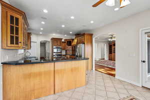 Kitchen with arched walkways, ceiling fan, recessed lighting, light tile floors, and wood cabinets