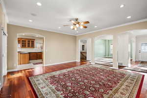 Unfurnished living room with crown molding, dark wood finished floors, recessed lighting, arched walkways, and a ceiling fan