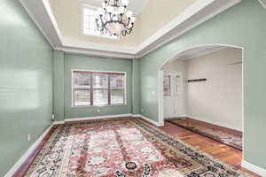 Entryway featuring wood finished floors, crown molding, arched walkways, a towering ceiling, and a chandelier