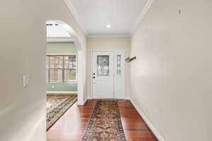 Entrance foyer with arched walkways, crown molding, and dark wood-type flooring