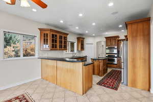 Kitchen with glass insert cabinets, a kitchen island with sink, recessed lighting wood cabinetry, and appliances with stainless steel finishes