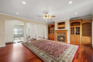 Living area with crown molding, arched walkways, dark wood-type flooring, recessed lighting, and a high end fireplace