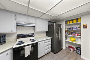 Kitchen with electric range, light countertops, stainless steel refrigerator with ice dispenser, backsplash, and light wood finished floors