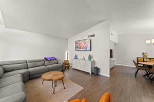 Living area with a chandelier, vaulted ceiling, and dark wood-style flooring