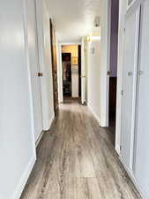 Hallway with a textured ceiling and wood finished floors