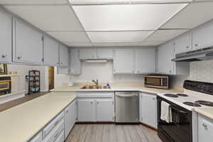 Kitchen featuring stainless steel appliances, light wood-type flooring, gray cabinetry, light countertops, and a paneled ceiling
