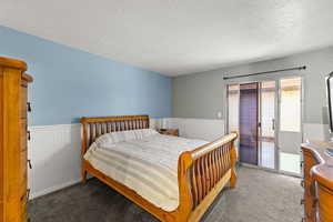 Bedroom featuring a textured ceiling, wainscoting, carpet flooring, and access to outside