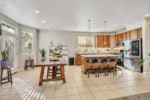 Kitchen with stainless steel appliances, brown cabinets, backsplash, hanging light fixtures, and a breakfast bar
