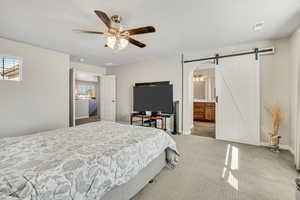 Carpeted bedroom with a barn door, ceiling fan, ensuite bath, and arched walkways
