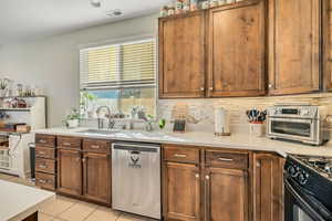 Kitchen featuring dishwasher, black gas range, backsplash, light tile patterned floors, and brown cabinetry